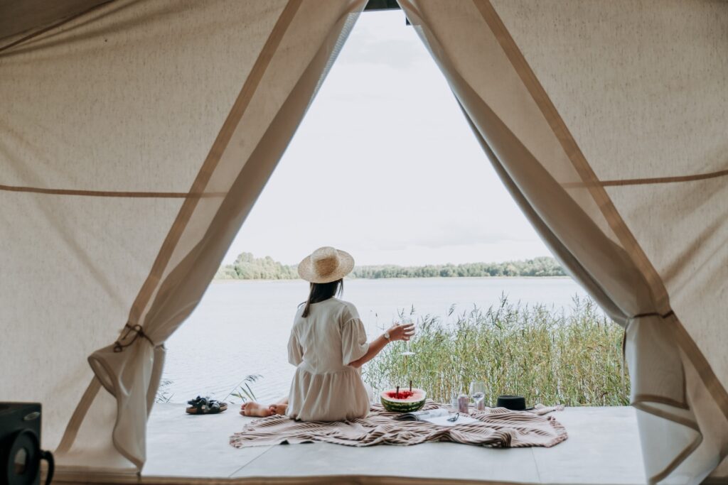 テントでくつろぐ女性。外には心地よい空と湖の自然の風景が広がっている。