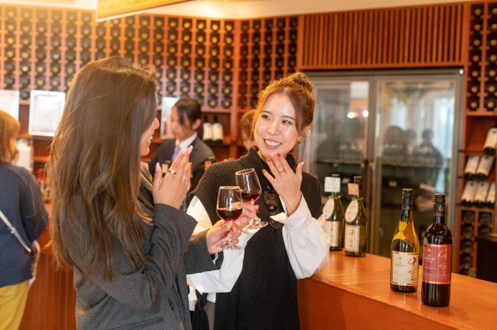 試飲会場で若い女性二人が赤ワインの試飲をしているところ。